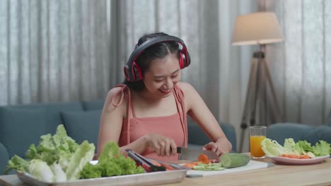 asian woman enjoys listening to music with headphones while slicing carrot at home