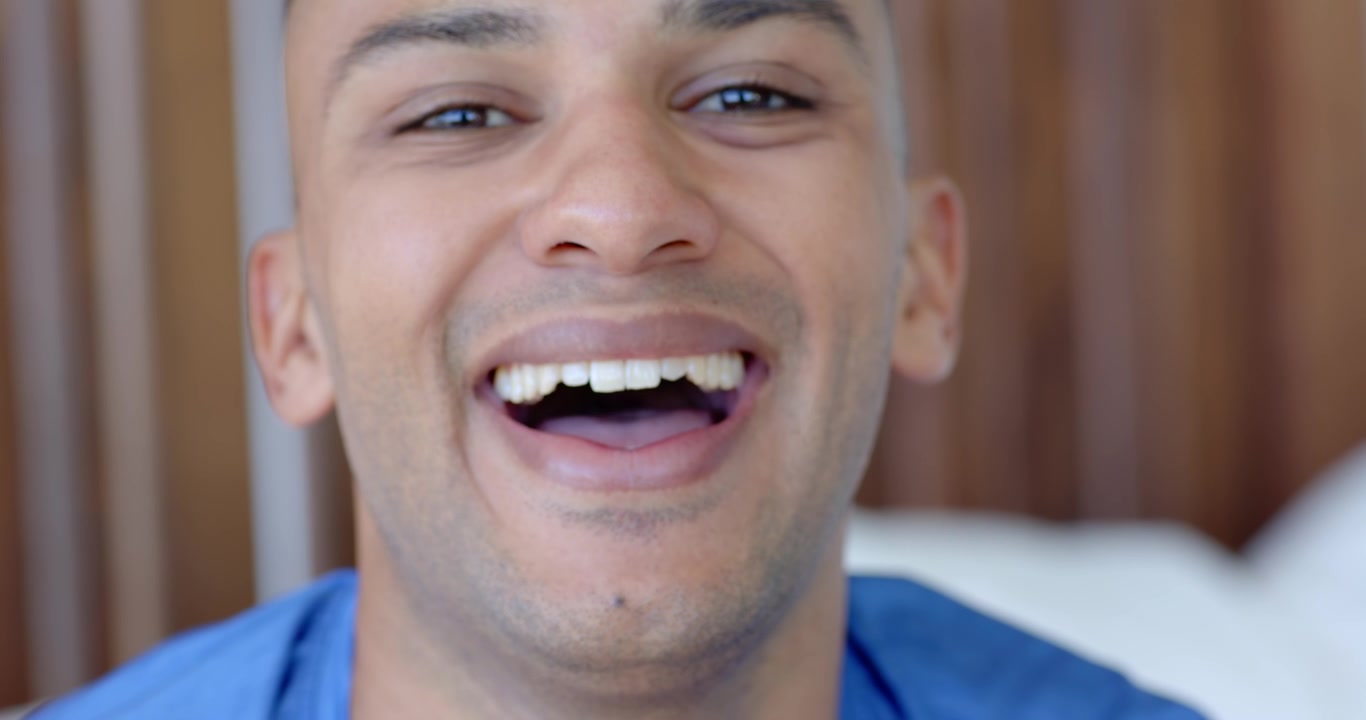 Adult man responding to prompt, shifting from neutral to laughing in bedroom headboard blue shirt