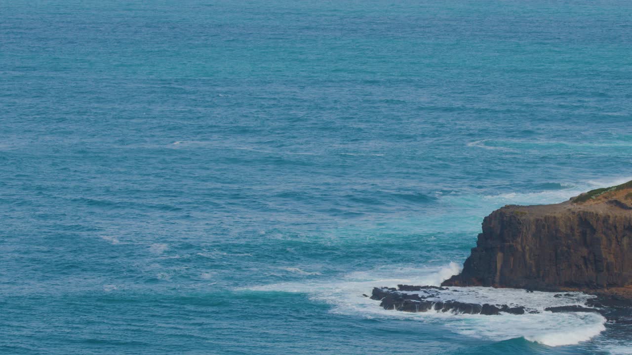 Steady wide shot of ocean waves hitting rugged cliffs under natural daylight, tranquil coastal landscape