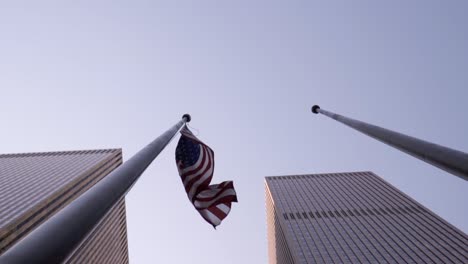 waving american flag in slow motion during sunny day in new york city manhattan. two skyscrapers from sixth avenue surrounding the usa flag.
