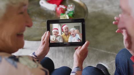 Smiling-senior-caucasian-couple-using-tablet-for-christmas-video-call-with-family-on-screen