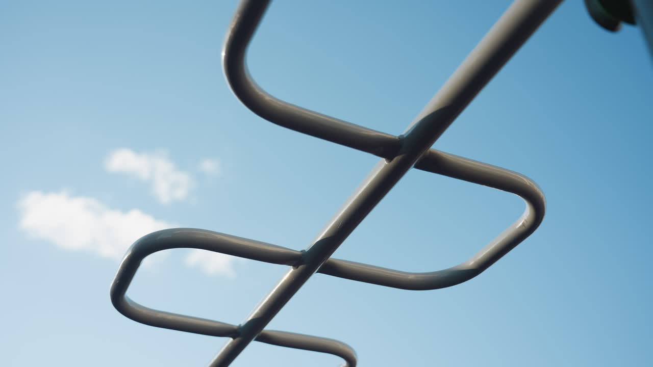 Sky view of silver colored outdoor monkey bars against clear blue sky, modern playground fitness equipment with hexagonal rungs and sturdy steel frame glistening under bright daylight
