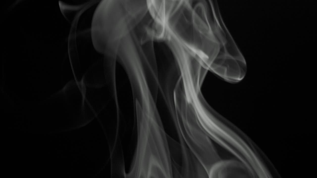 Nuvole di fumo grigio che salgono lentamente con eleganti volute verso l'alto. Fumo di sigaro in bianco e nero che sale dal basso verso l'alto. Primo piano, isolato su sfondo nero