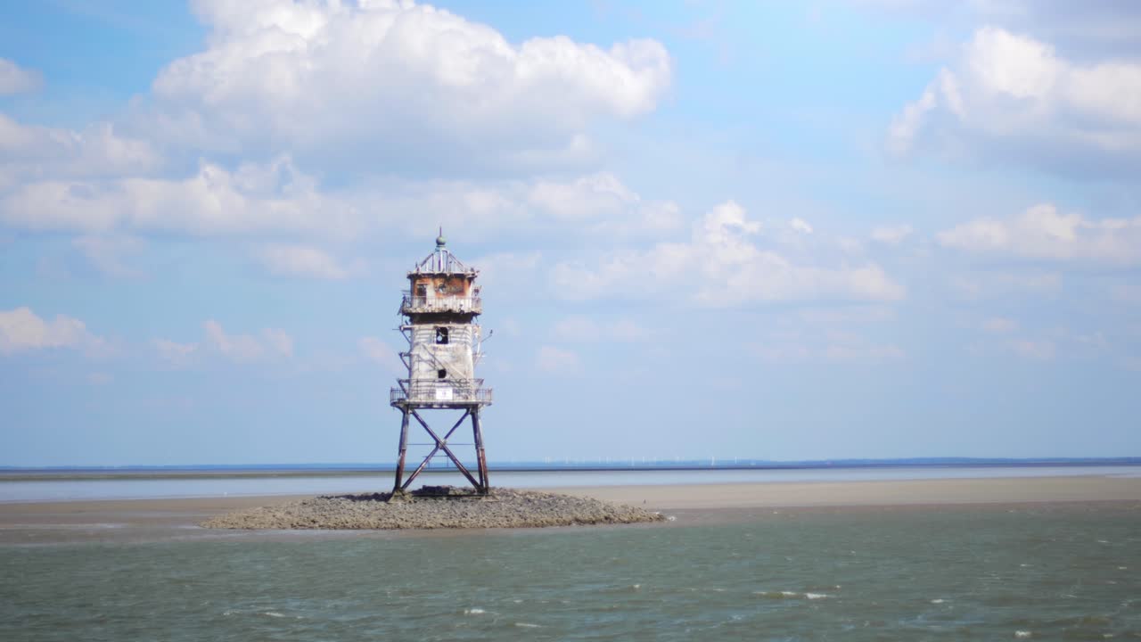 Old abandoned lighthouse called cormoran tower in the wadden sea with water flowing beneath and a cloudy sky.