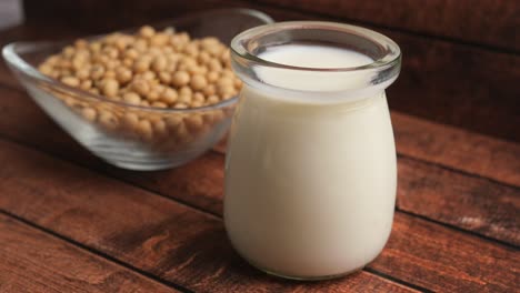 fresh soy milk in a glass jar with soybeans on a wooden background