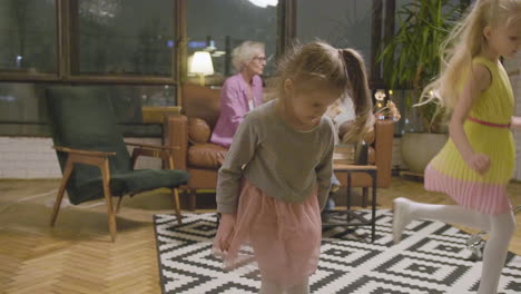 two little sisters playing in the living room while their two grandmothers talking on sofa