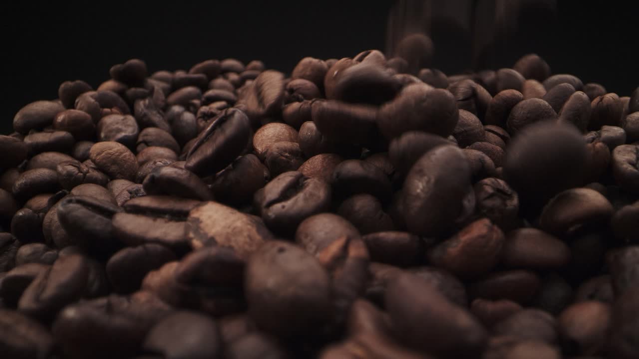 Macro footage of falling coffee beans on black background. Real time