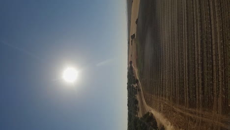 tracking vertical format aerial: moto on dirt road beside farm field