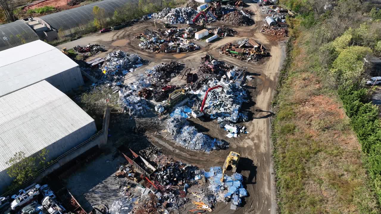 Working excavate on scrapyard on sunny day. Aerial flyover shot. Transporting metal and old scrap iron on industrial area