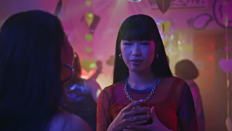 Party woman holding cocktail glass at vibrant club closeup. Chinese girl dancing