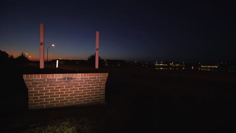 algunos coches pasan a toda velocidad por un cartel iluminado en blanco por la noche junto a la carretera cerca de la puesta de sol