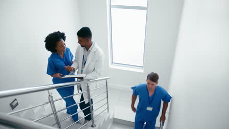 male doctor and female nurse with clipboard discussing patient notes on stairs in hospital building