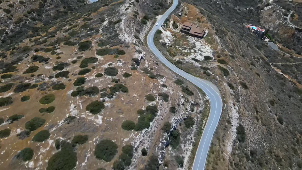Aerial view of a winding switchback road cutting through arid hills above Durrës, Albania. Rugged terrain meets human engineering, with sparse vegetation and distant residential clusters
