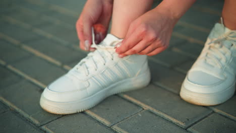 close-up of individual tying shoelaces of white sneakers on interlocked pavement path, detailed shot showing hands firmly adjusting laces