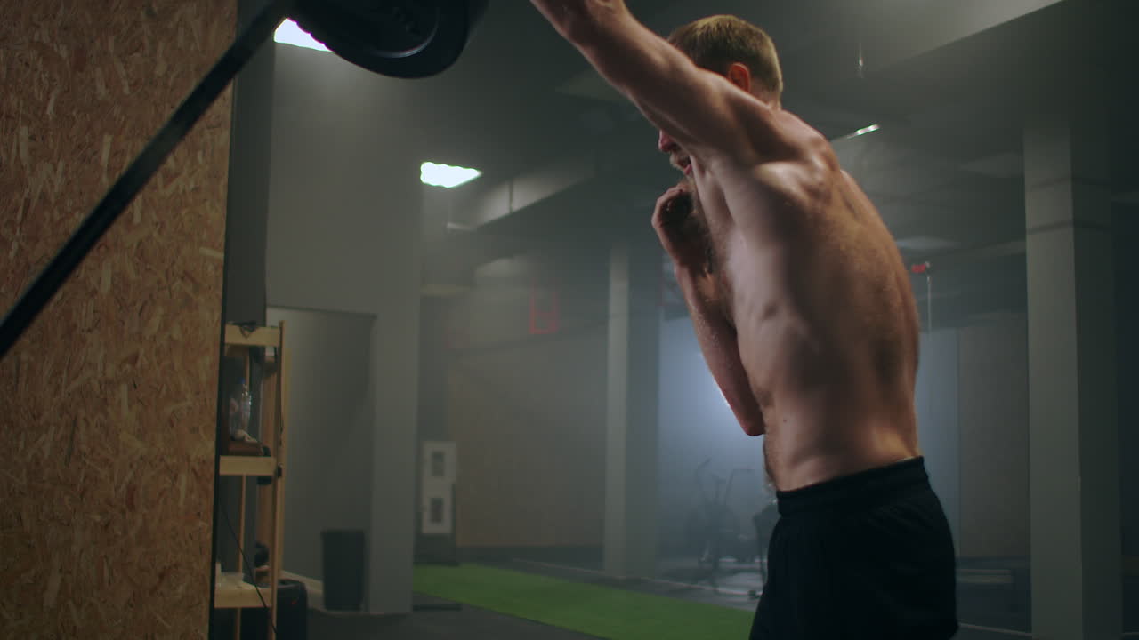 남성 운동 선수 는 한 손 으로 무게 바 를 느린 움직임 으로 들어 올린다. 권투 선수 의 힘 훈련. 그 남자 는 체육관 에서  ⁇  을 흘리며 손 으로 타격 의 힘 을 연습 하고 있다