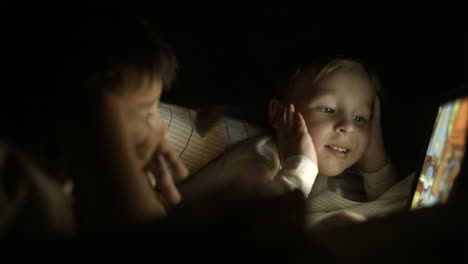 two boys lying in bed at night and using pad