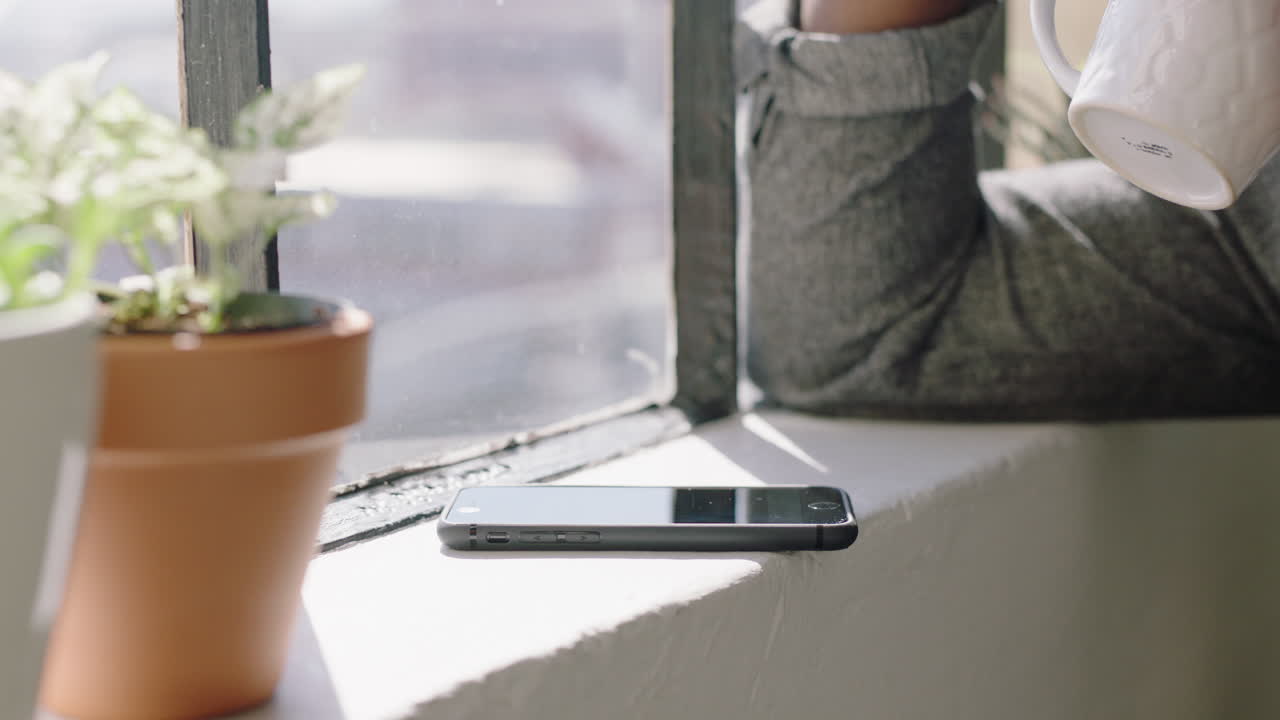 스마트폰을 사용하는 젊은 아프리카계 미국인 남자가 집에서 커피를 마시고 메시지를 검색하고 네트워크를 구축하고 소셜 미디어를 공유하고 라이프 스타일을 온라인으로 즐기고 현대적인 아파트에서 긴밀하게 휴식을 취하고 있습니다.