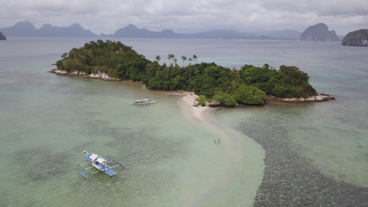 Movimiento orbital aéreo de dron alrededor de una isla tropical con un banco de arena blanca en Palawan, Filipinas, mostrando agua cristalina y un pintoresco paisaje para el salto de islas.