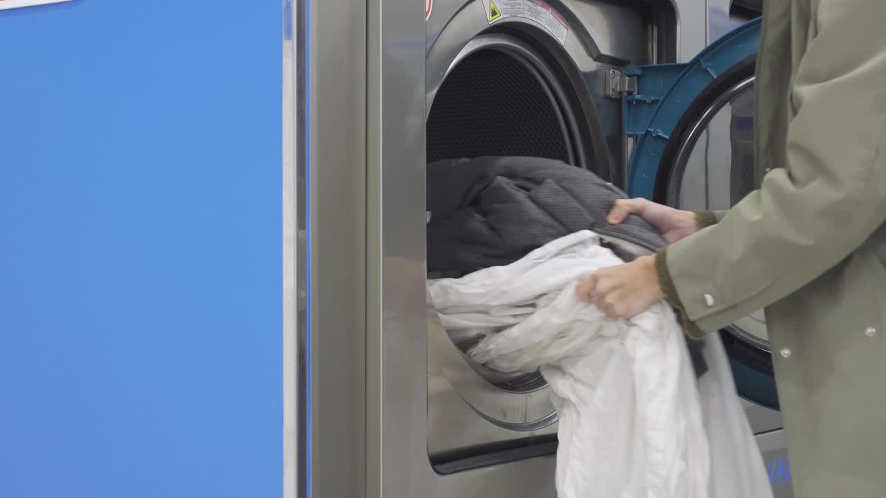 Close-up footage of hands pulling out freshly washed wet clothes from a professional self-service washing machine in a public laundry facility