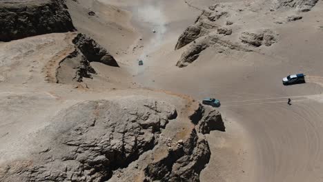 Drone-Shot-of-Trucks-driving-through-a-canyon-in-the-desert-in-caravan-through-rocky-dry-terrain
