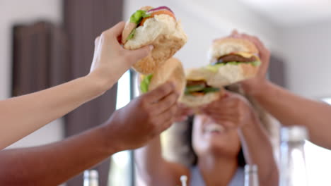 diverse friends toasting with burgers, celebrating and enjoying food together indoors