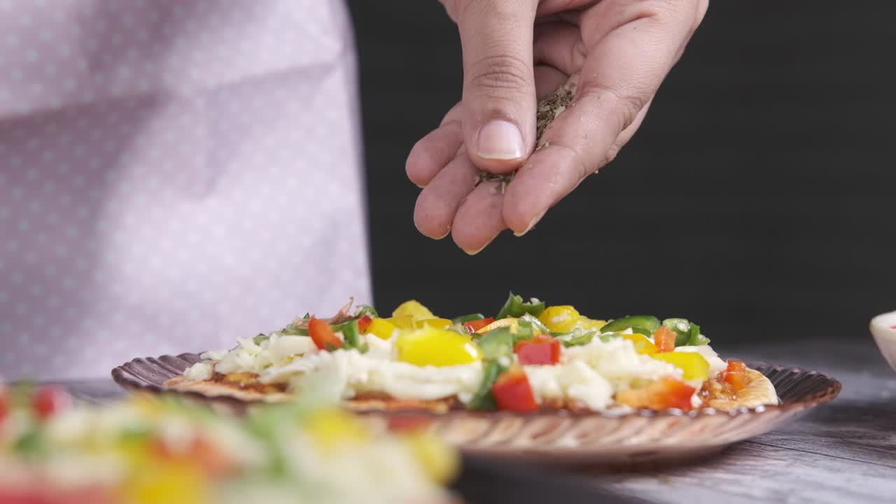una mujer rociando hierbas en una pizza.