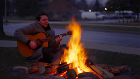 man playing guitar by a campfire