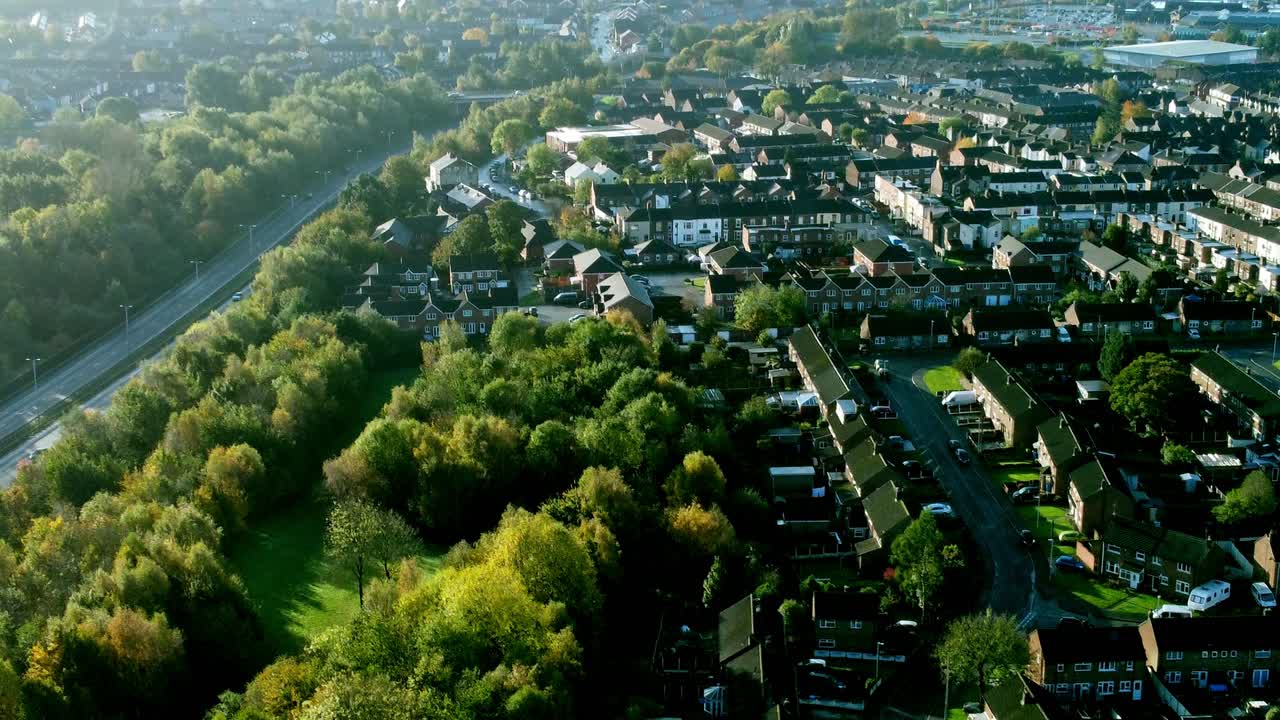 Aerial view tilt down above countryside dual carriageway traffic country road between woodland treetop at sunrise towards Widnes town