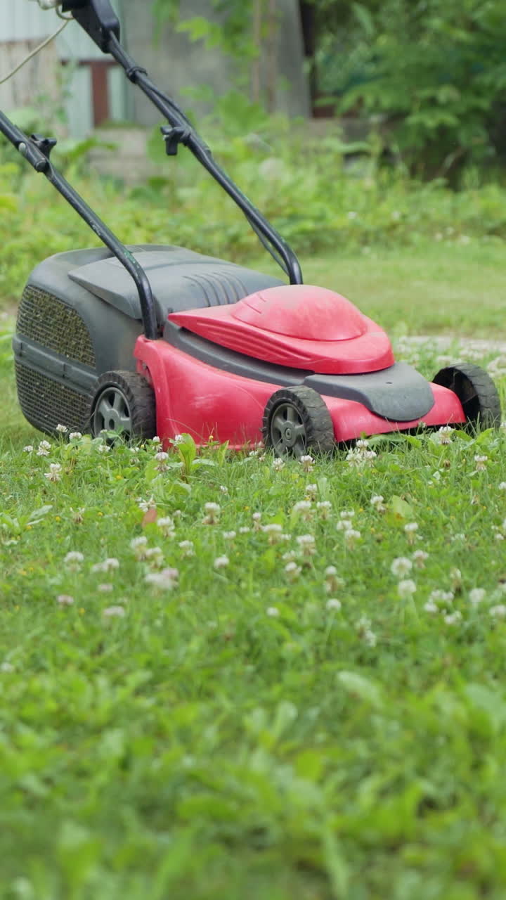 man is working with lawn mower in the yard in the summer. Lawn mower is mowing grass on the plot Vertical video