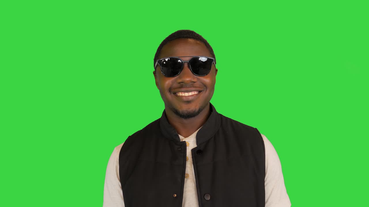 Homem afro-americano feliz colocando seus óculos de sol e sorrindo em uma Tela Verde, Chroma Key.