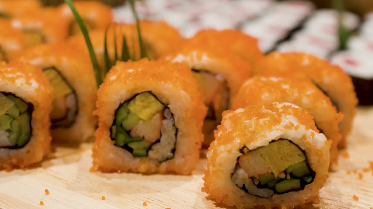 Lähikuva metallipihdeistä valitsemassa California-rullaa japanilaiselta buffet-vadilta
