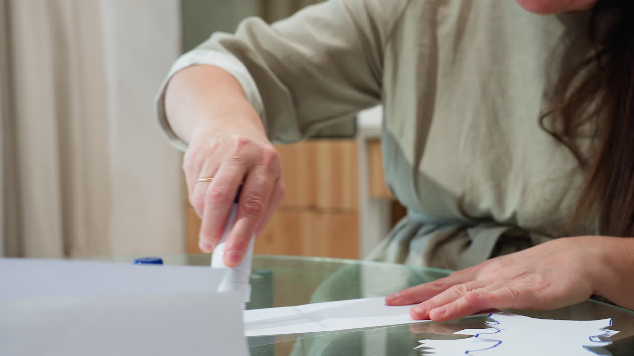 Hand view of woman applying liquid glue on paper and then joining the paper together, focus on crafting activity with a calm home setting and blurred background