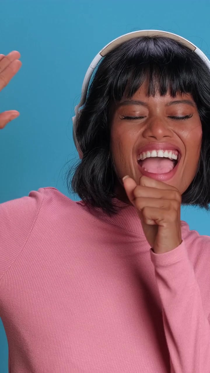 Happy south asian woman in wireless headphones enjoying music and dancing on