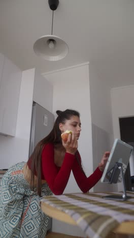 woman eating apple and using tablet in kitchen