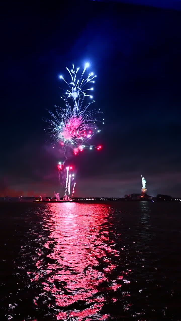 New York, USA, 1 August 2025: Fireworks over the dark waterscape at night. Statue of Liberty nearby. 4th July in New York, USA. Vertical video