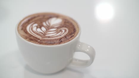 Weiße-Latte-Art-Blume-In-Weißer-Teetasse-Auf-Weißem,-Glänzendem-Tisch