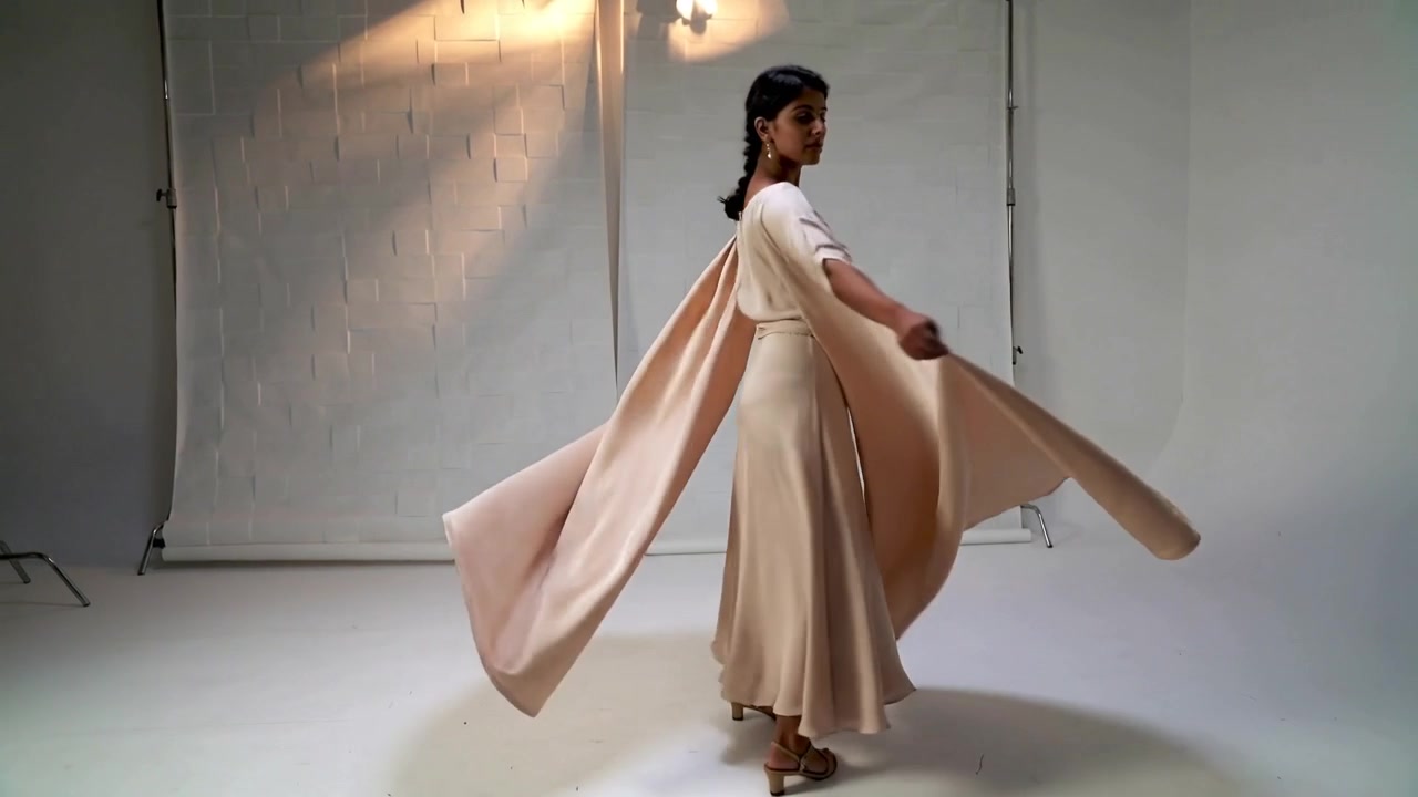 Drejer på kommando, indisk model i høje hæle holder kappe-kanter, fremviser beige kjole i studie.