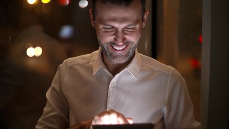 Primer-Plano-De-Un-Hombre-Sonriente-Usando-Una-Tableta-Por-La-Noche