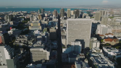 Toma-Aérea-Del-Centro-De-La-Ciudad-Y-La-Bahía-Del-Mar-En-Segundo-Plano.-Los-Delanteros-Vuelan-Por-Encima-De-Los-Edificios-Altos-De-La-Ciudad.-Ciudad-Del-Cabo,-Sudáfrica