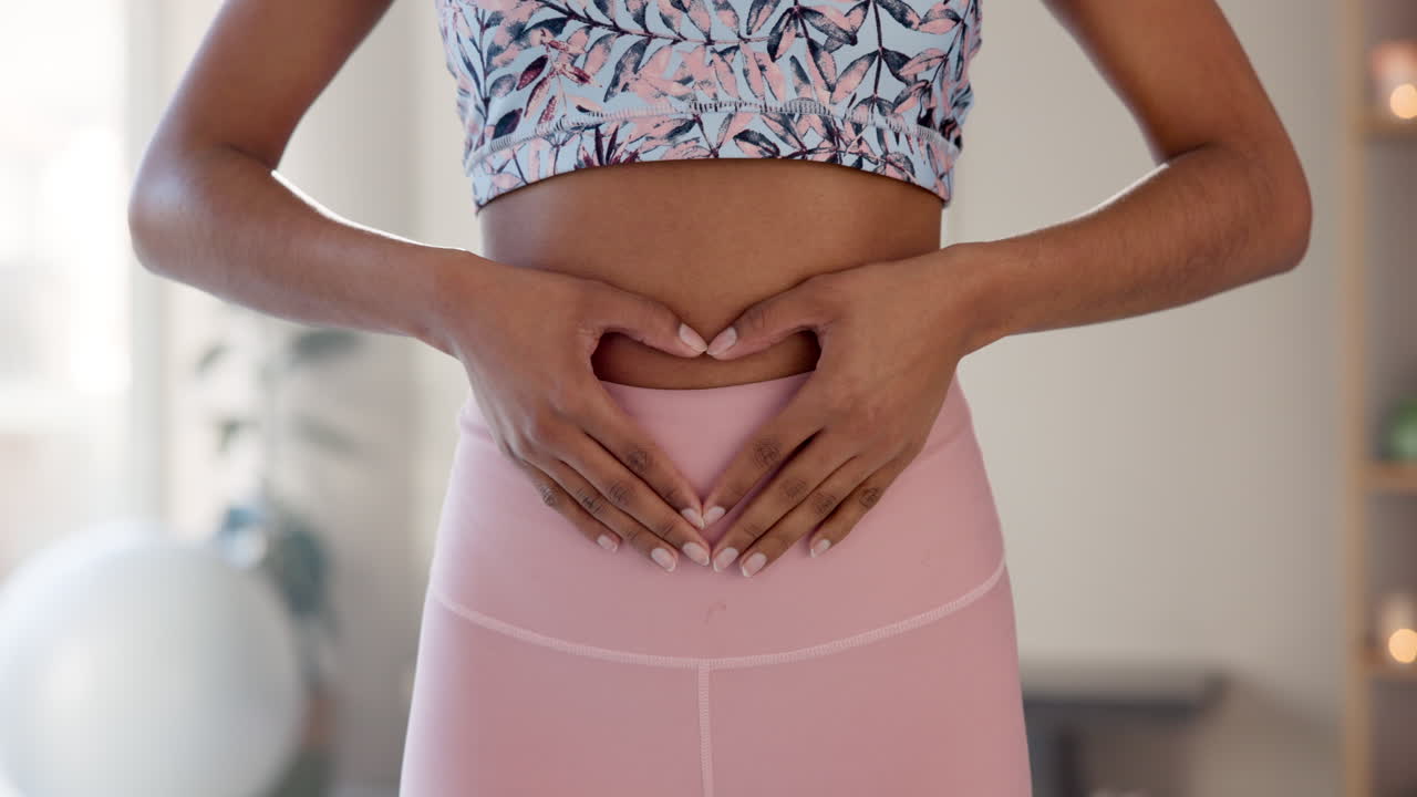 Woman making heart shape with hands on belly