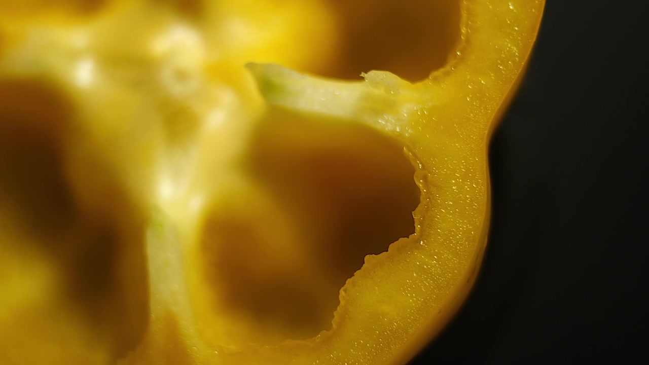 Toma cenital con lente macro de 50p de una rodaja de pimiento amarillo girando para revelar textura, semillas y color natural vibrante.