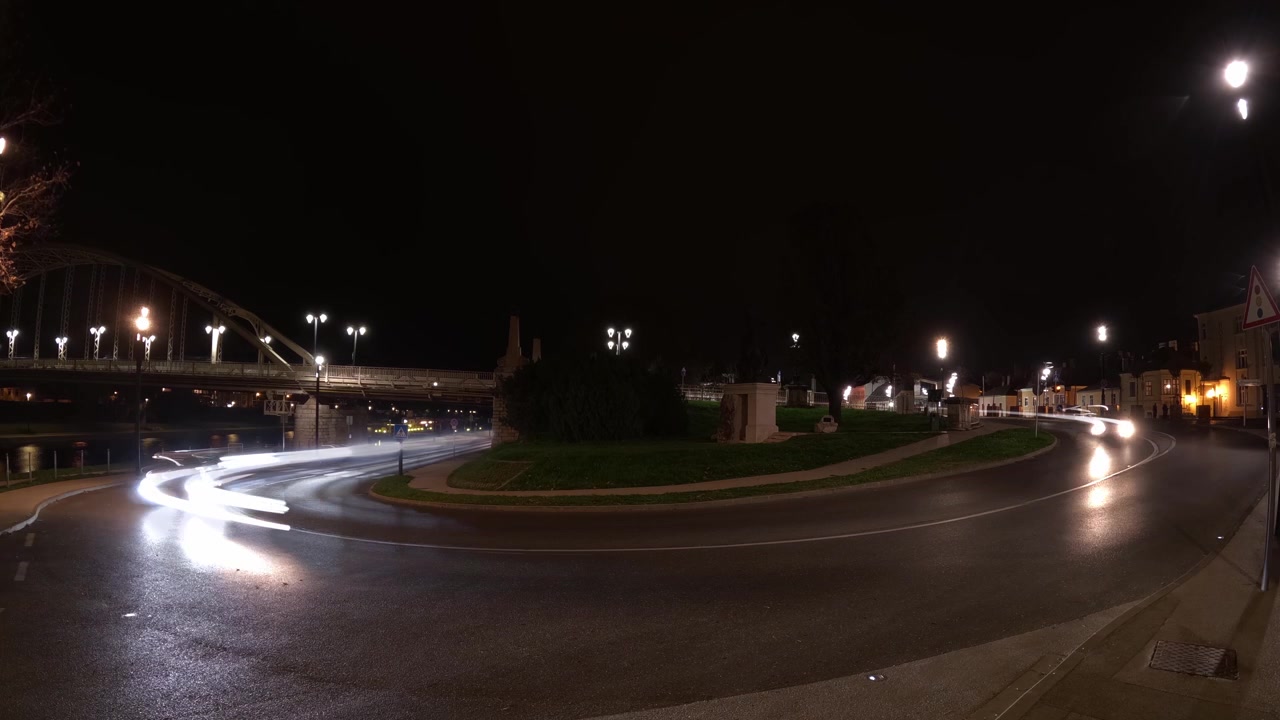 Time lapse di scie luminose di veicoli in movimento lungo una strada curva vicino a un ponte, illuminate dai lampioni di notte accanto al ponte