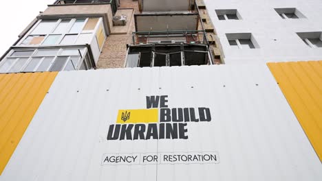 a metal fence with "we build ukraine" by the state agency for reconstruction surrounds a war-damaged building in irpin, ukraine, hit by russian missiles during the ukraine-russia conflict.