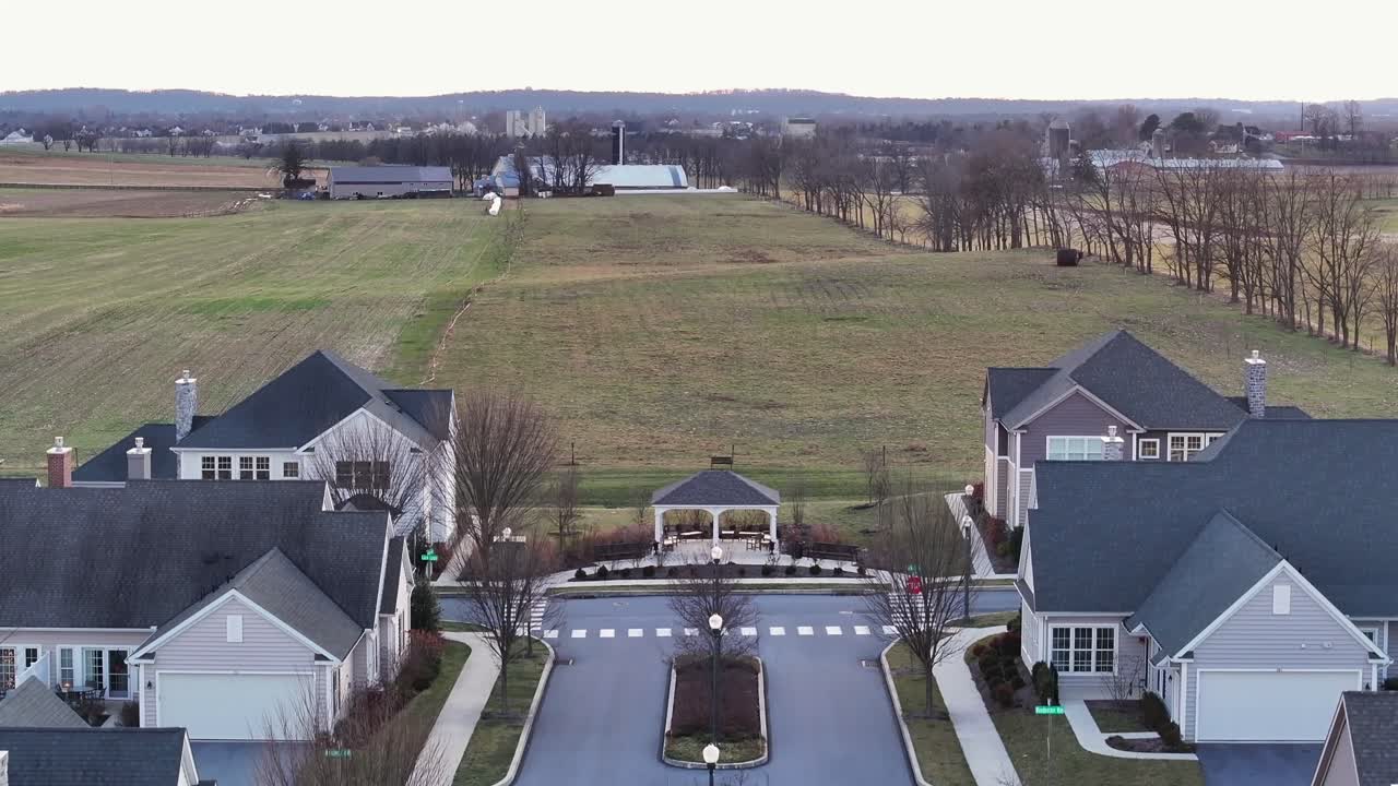 Luxury Neighborhood border to agricultural farm fields and farm house in distance. Sunset twilight scene in american suburb. Rising drone wide shot. Pennsylvania, America.