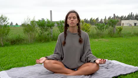 young woman sits and meditates in lotus pose on grass lawn on cloudy day