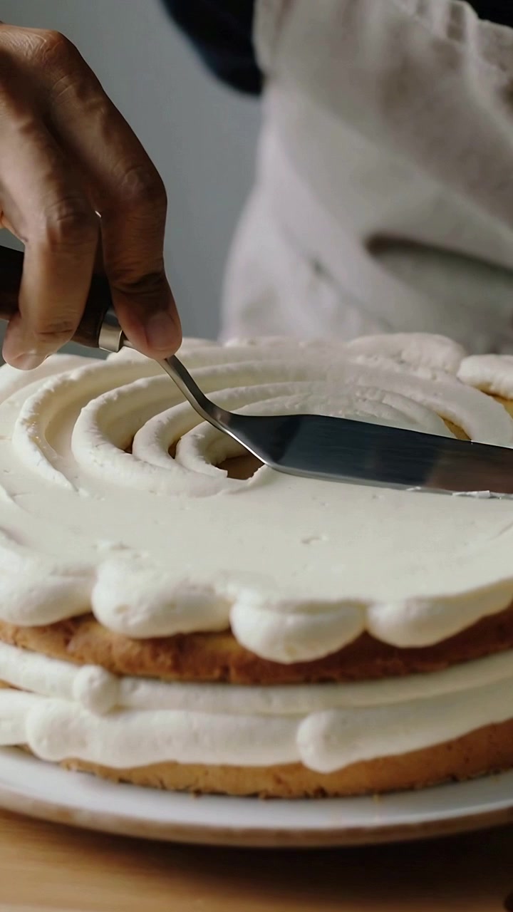 Vertical video: Finishing hand pressing spatula onto spiral on 2-layer cake at home with apron
