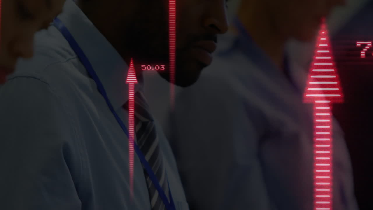 Man analyzing finance data with colleagues on trading floor, red arrows rising and ticker updating