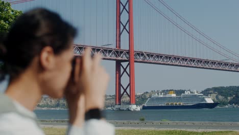 mujer fotografiando un crucero y un puente en lisboa, portugal