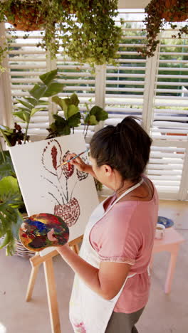 vertical video: painting on canvas, woman using palette and brush in home studio