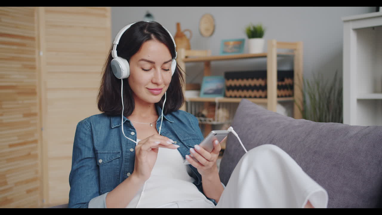 여성이 헤드폰과 전화로 소파에서 휴식을 취하고 있습니다.